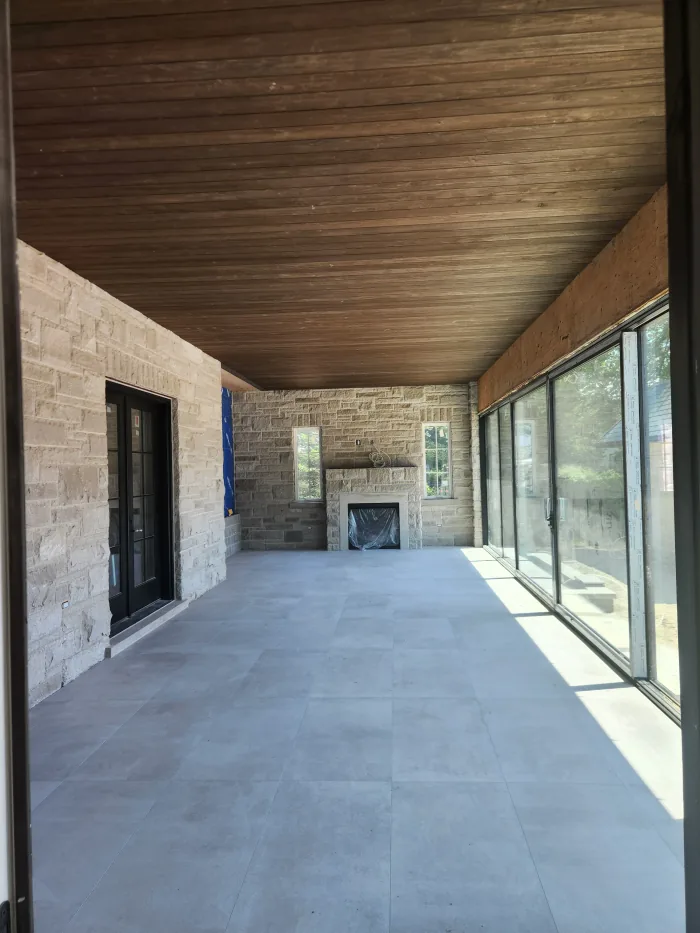 Covered loggia by Sigma Painting — stained tongue-and-groove ceiling over stone walls and an outdoor fireplace