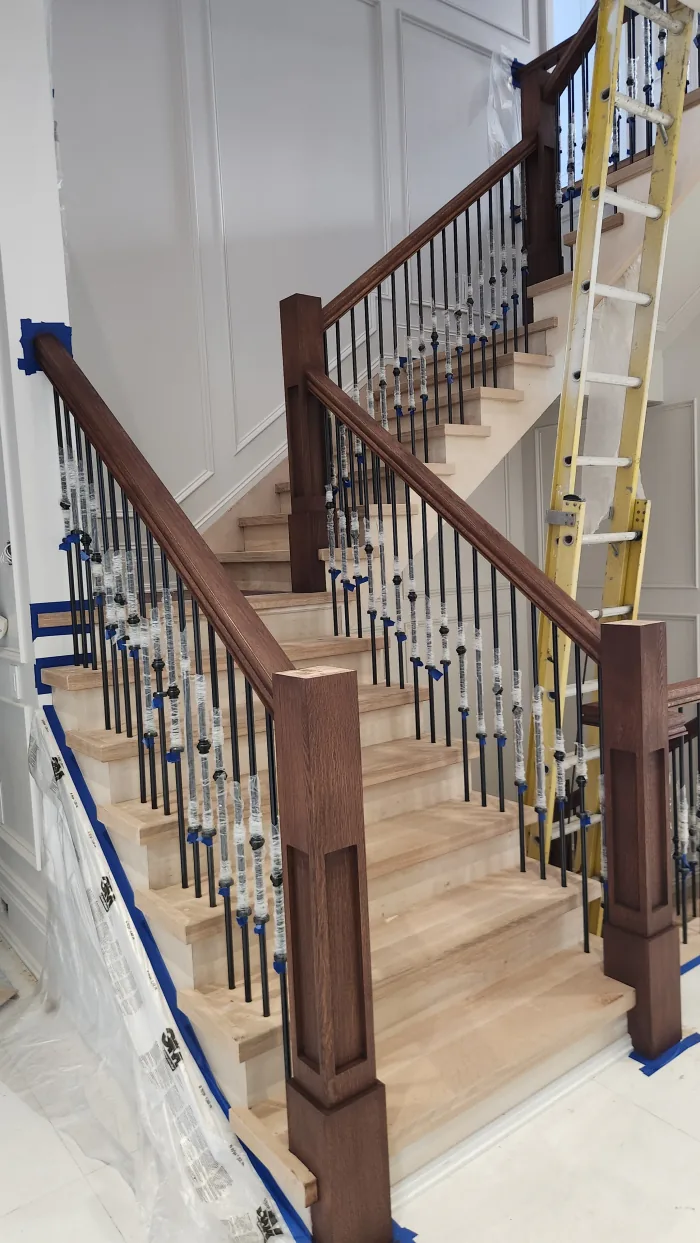 Stair staining in progress by Sigma Painting — handrail and posts stained, spindles wrapped for protection