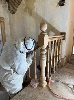 Stair refinishing preparation by Sigma Painting — a worker preparing a turned wood newel post and balustrade