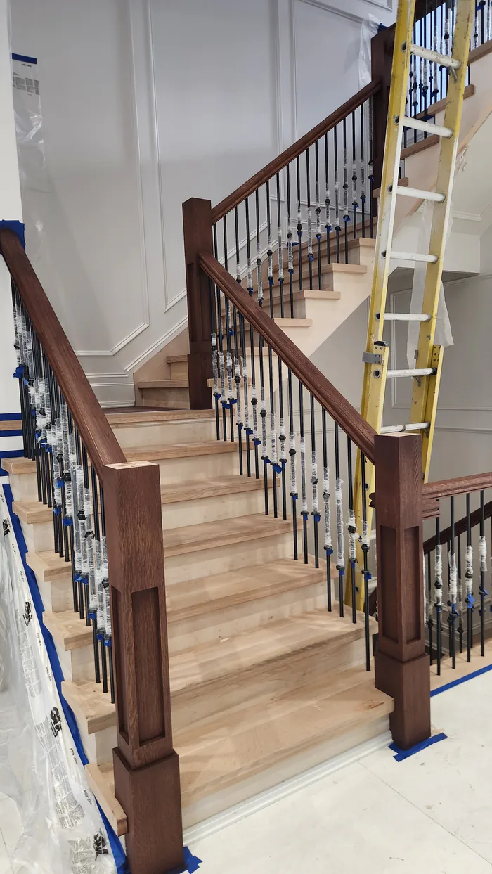 Stair staining in progress by Sigma Painting — brown-stained handrails and newel posts with individually wrapped iron spindles
