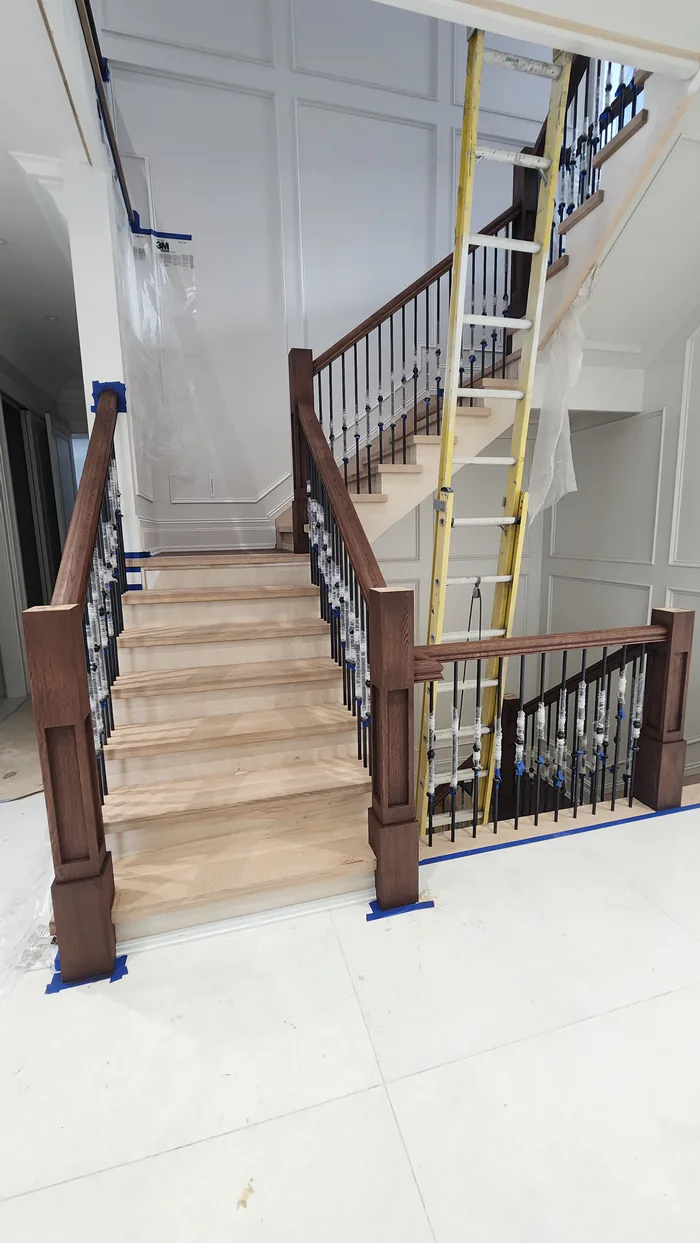 Stair staining in progress by Sigma Painting — staircase and lower landing with stained posts, wrapped spindles and protected floors
