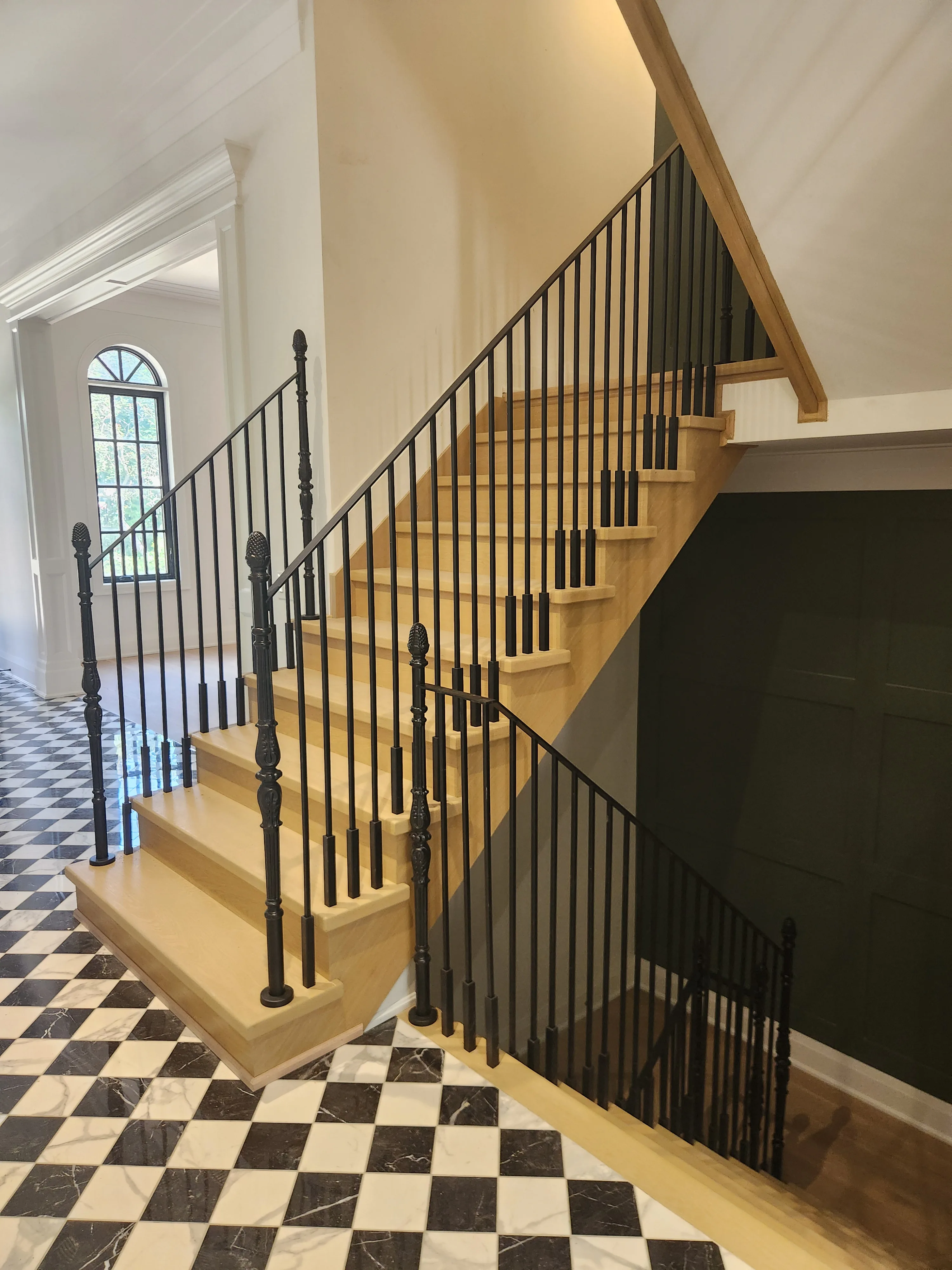 Stair staining by Sigma Painting — oak treads and iron spindles above a checkerboard marble floor