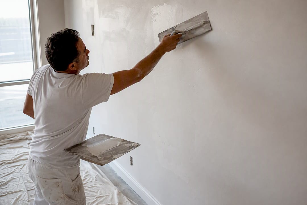 Worker applying skim coat to new drywall